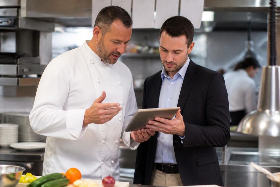 A chef and a business partner looking at a tablet together in a kitchen